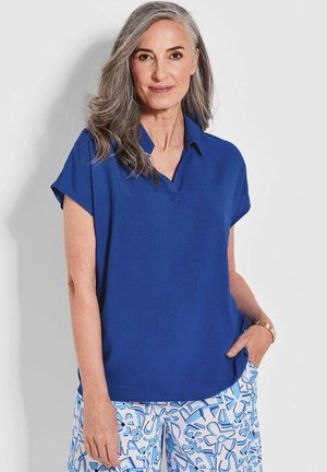 Blouse bleue à manches courtes avec un décolleté en V et une texture lisse et légère. Associée à un pantalon bleu clair à motifs avec des designs abstraits.