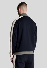 Felpa blu navy con colletto grigio e strisce color crema sulle spalle. Tessuto morbido, vestibilità rilassata e polsini a coste.