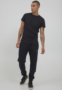 Svart bomull T-skjorte med brystlomme, kombinert med svarte joggebukser med hvit sidepanel og elastiske mansjetter. Svarte joggesko.