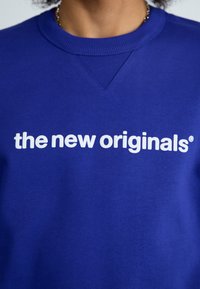 Felpa blu in misto cotone. Caratterizzata da un colletto a girocollo e polsini a costine. Sul davanti, un testo bianco recita "the new originals®" in modo prominente.