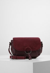 Bordeauxrode leren en suède crossbodytas met een ronde metalen accent, klep met sluiting en verstelbare riem. Zachte textuur, compacte vorm.