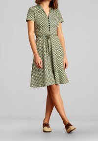 Zielona sukienka w wzory z krótkimi rękawami, zapinana na guziki, z wiązanym w talii detalem; zestawiona z brązowymi butami na sznurówki.