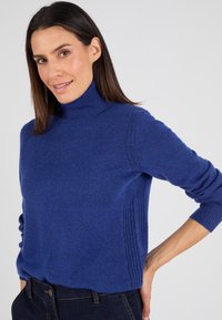 Blauw coltrui gemaakt van zacht materiaal, met geribbelde details aan de zijkanten en lange mouwen, aangevuld met een ontspannen pasvorm.