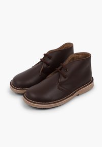 Hnědé kožené kotníkové boty s kulatými špičkami, vybavené dvěma oky pro tkaničky, prošitými detaily a světlými hnědými gumovými podrážkami.