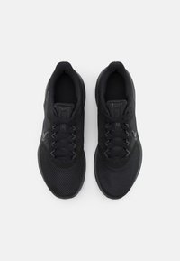 Zapatillas deportivas negras con parte superior de malla, puntera reforzada y cordones planos. Destaca el logo en forma de swoosh y la suela texturizada.