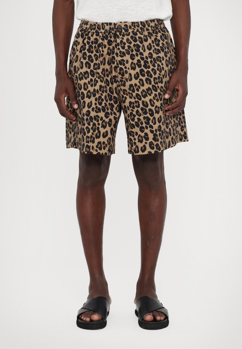 Leopard-print shorts in tan and black, made from lightweight fabric, with an elastic waistband and a relaxed fit, paired with black sandals.