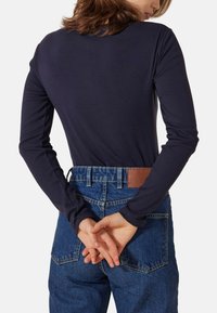 Marineblaues Langarmoberteil mit figurbetontem Schnitt, kombiniert mit hoch taillierten blauen Jeans mit braunem Lederpatch und sichtbaren Nahtdetails.