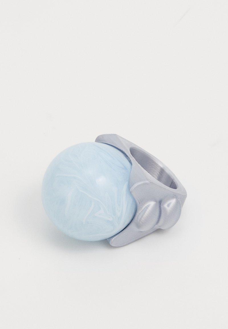 Anillo de metal con un centro esférico de color azul claro veteado, que presenta una banda de tono plateado y un acabado suave y pulido.