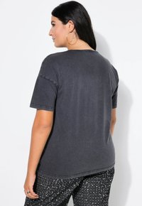 Donkergrijze katoenen t-shirt met een ronde halslijn en korte mouwen, met contrasterende stiksels. Geweven zwarte broek met pailletten.