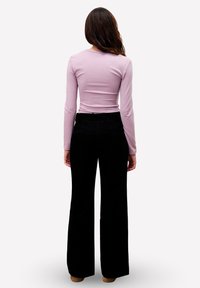 Chemise à manches longues lavande avec un design ajusté, associée à un pantalon large taille haute noir. Tissu lisse et coutures arrière visibles.