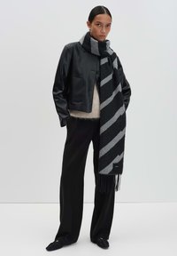 Zwarte leren cropped jack, beige gebreide top, zwarte brede broek, grijs en zwart gestreepte sjaal met franjes, en zwarte instappers.