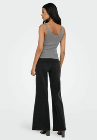 Top sin mangas gris acanalado con espalda en V, combinado con unos pantalones vaqueros negros de campana de cintura alta, que presentan un diseño clásico de bolsillo y tacones texturizados.