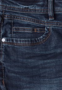 Jeans de denim azul oscuro con un diseño clásico de cinco bolsillos, que cuentan con costuras visibles, un botón de metal y un ligero desgaste en la textura.
