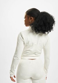 Top blanc à manches longues avec un motif paisley, tissu doux et design court. Assorti avec un bas taille haute.