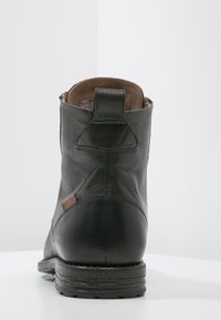 Stivale alla caviglia in pelle nera con punta arrotondata, dettagli cuciti e rivestimento in tessuto marrone. Presenta un comodo pull-tab sul retro.