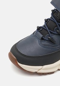 Baskets navy et noires avec un dessus lisse, des accents en caoutchouc texturé, une semelle grise et des lacets élastiques intégrés dans le design.