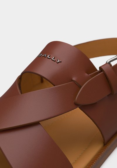 Καφετί δερμάτινο σανδάλι με φαρδιές λουρίδες, ασημί λογότυπο Bally και ρυθμιζόμενο πόρπη σε ταμπά μαλακό πέλμα.