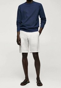 Navy knit sweater with a round neck, paired with white linen shorts. The model wears black flip-flops. Simple, casual style.