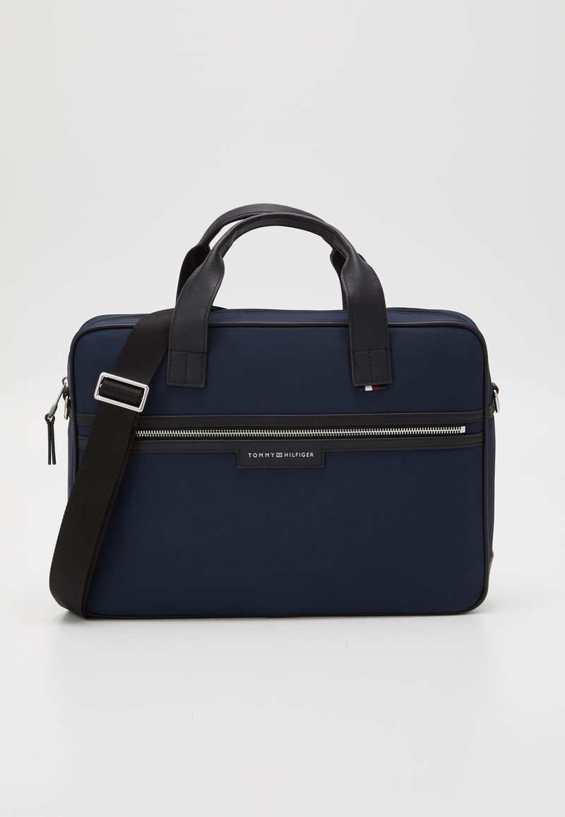 Mallette rectangulaire bleu marine avec poignées noires, bandoulière réglable, poche zippée avant et écusson du logo Tommy Hilfiger.