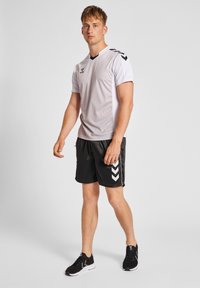 Hvid athletic T-shirt med tekstureret mønster og sorte accenter, parret med sorte shorts med hvide v-formede striber, båret med sorte sneakers.