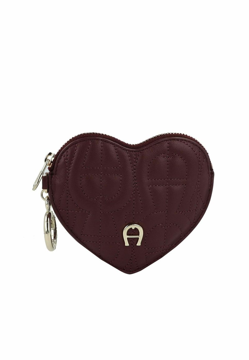 Portefeuille en cuir bordeaux en forme de cœur, texture matelassée, fermeture éclair et éléments en métal doré, avec un logo décoratif sur le devant.