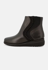 Stivale alla caviglia in pelle nera con finitura liscia, pannelli laterali elasticizzati e borchie decorative lungo la cucitura curvata. Leggero soletta a cuneo.