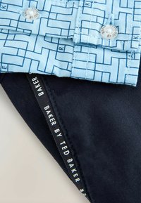 Niebieska koszula w wzory o geometrycznym wzorze, połączona z granatowym fragmentem materiału. Posiada metkę z logo "BAKER BY TED BAKER."