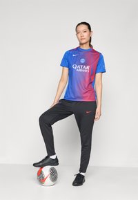 Modrá a červená prechodová dres Nike s logom Qatar Airways, čierne športové nohavice Nike, čierne športové topánky a futbalová lopta s čierno-bielym vzorom.