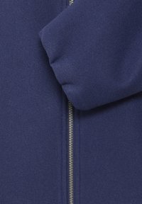 Tums zilas krēsls ar gludu tekstūru, rāvējslēdzis visā garumā un piedurkņu detalizācija ar aproci.