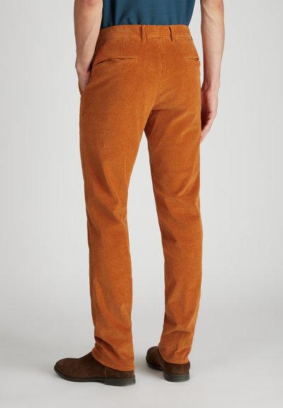 Pomarańczowe spodnie dżinsowe o prążkowanej fakturze, dopasowany krój, z dwiema tylnymi kieszeniami, w połączeniu z brązowymi zamszowymi botkami za kostkę.
