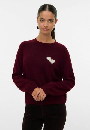 Pull bordeaux avec un col rond et des manches longues. Présente un motif de cœur blanc sur la poitrine. Fabriqué en matériau doux et texturé.