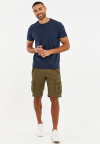 Marineblaue Baumwoll-T-Shirt, kombiniert mit olivgrünen Cargo-Shorts mit mehreren Taschen, abgerundet mit weißen Sneakers. Einfaches lässiges Outfit.