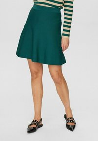 Vihreä levenevä hame, jossa on sileä kangas ja istuva vyötärö. Yhdistetty teräväkärkisiin mustiin kenkiin, joissa on leikattuja yksityiskohtia ja niittejä.