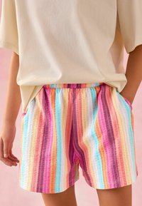 Shorts rayés multicolores en tissu texturé avec des teintes de rose, violet, bleu et jaune, une taille élastique et des poches latérales.