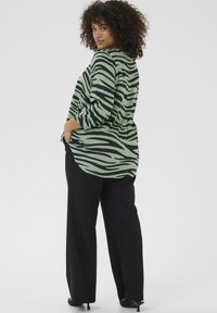 Blusa a righe verdi e nere con vestibilità ampia, maniche a tre quarti e orlo curvo, abbinata a pantaloni neri.