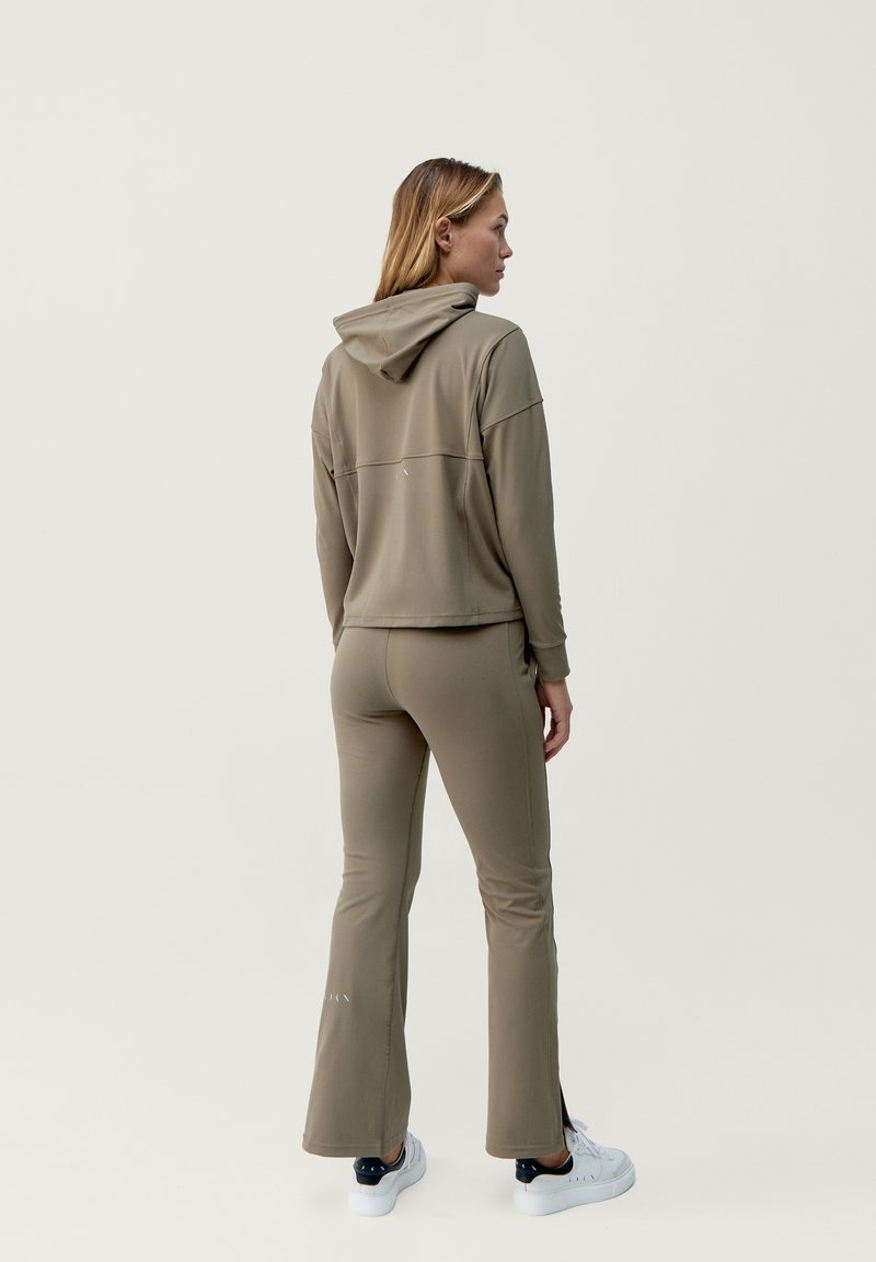 Khaki Athleisure-Set mit einem verkürzten Hoodie und ausgestellten Hosen, hergestellt aus weichem, dehnbarem Material mit einer glatten Textur. Weiße Akzentdetails sichtbar.