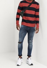 Red and navy striped ribbed sweater, distressed dark blue skinny jeans, and white athletic shoes. Black crossbody bag.