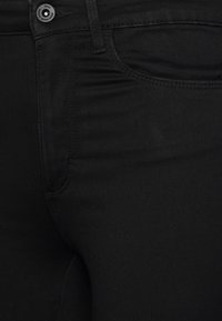 Zwarte spijkerbroek van denim met een gladde textuur, slim fit, opvallende zijnaad en knoopsluiting met de merknaam zichtbaar.