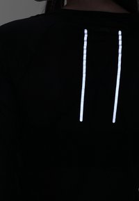 Camiseta atlética de malla negra con dos franjas reflectantes verticales en la parte posterior para mayor visibilidad. Tejido transpirable con un acabado texturizado.