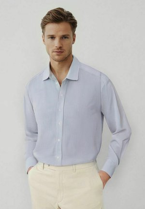 Chemise de dress à rayures bleu clair avec un col classique, un boutonnière à l'avant et des manches longues. Portée avec un pantalon beige pour une apparence formelle.