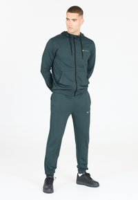 Mörkgrön zip-up hoodie med justerbar dragsko, två framfickor, parat med matchande joggers med en logotyp och elastiska ärmslut.