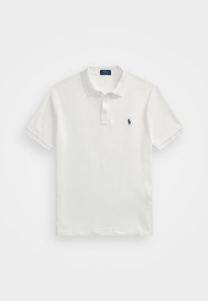 Valkoinen puuvillapolo-paita, jossa on klassinen malli, lyhyet hihat, kolme nappia sekä pieni laivastonsininen logo vasemmassa rinnassa.