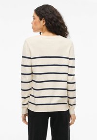Kremowy sweter z granatowymi poziomymi paskami, wykonany z miękkiego materiału, z okrągłym dekoltem i długimi rękawami.