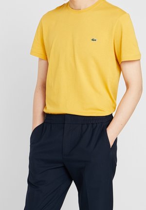 Żółta bawełniana koszulka z krótkim rękawem, z małym zielonym logo. W zestawie z granatowymi spodniami z elastycznym pasem.