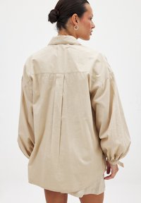 Béžová oversize košeľa z ľahkej tkaniny, s rázporkom na chrbte, gombíkovými rukávmi a golierom.