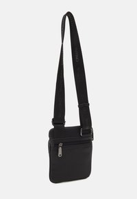 Malá černá kabelka přes rameno s nastavitelným popruhem, vyraženým logem Valentino a přední kapsou na zip, minimalistický design.