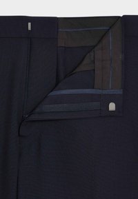 Granatowe spodnie z zamkiem błyskawicznym, pasem z czarnymi i niebieskimi akcentami oraz gładkim, teksturowanym wykończeniem materiału.