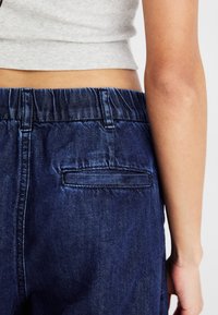 Pantalones cortos de mezclilla azul oscuro con cintura elástica, que cuentan con un solo bolsillo trasero y una textura suave.