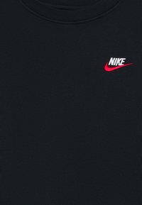 Svart stoff med en liten brodert hvit Nike-logo og rød swoosh nær halslinjen.