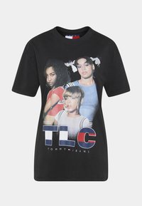 Black cotton t-shirt featuring a graphic print of three individuals with "TLC" and "TOMMY JEANS" text below, short sleeves, and a crew neckline.